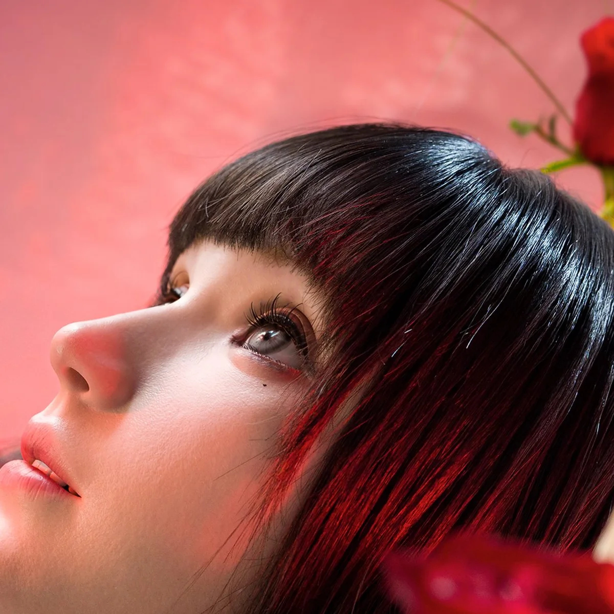 Origin F1 med mørkt hår vist i profil blandt røde blomster. Producentmateriale: AheadForm.