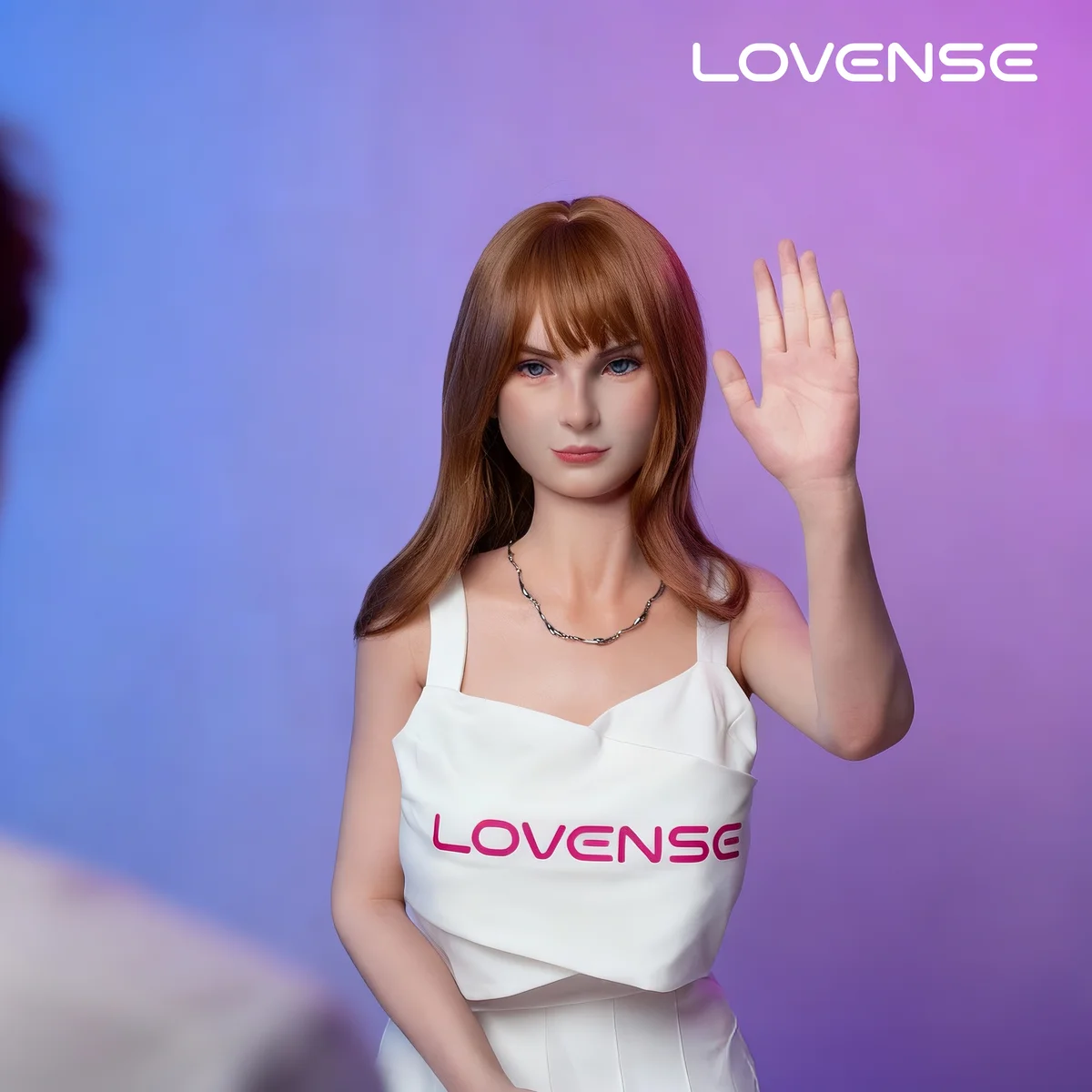 Lovense AI Doll med løftet hånd over for en person. Producentbillede fra CES2026-pressekittet; revisionen er ikke verificeret.